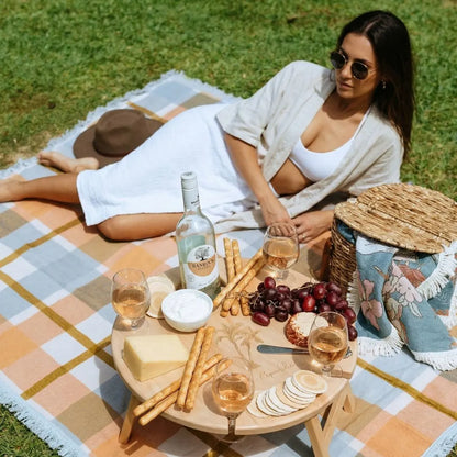 Woman sitting on a picnic blanket with a table of food and drinks in a grassy area