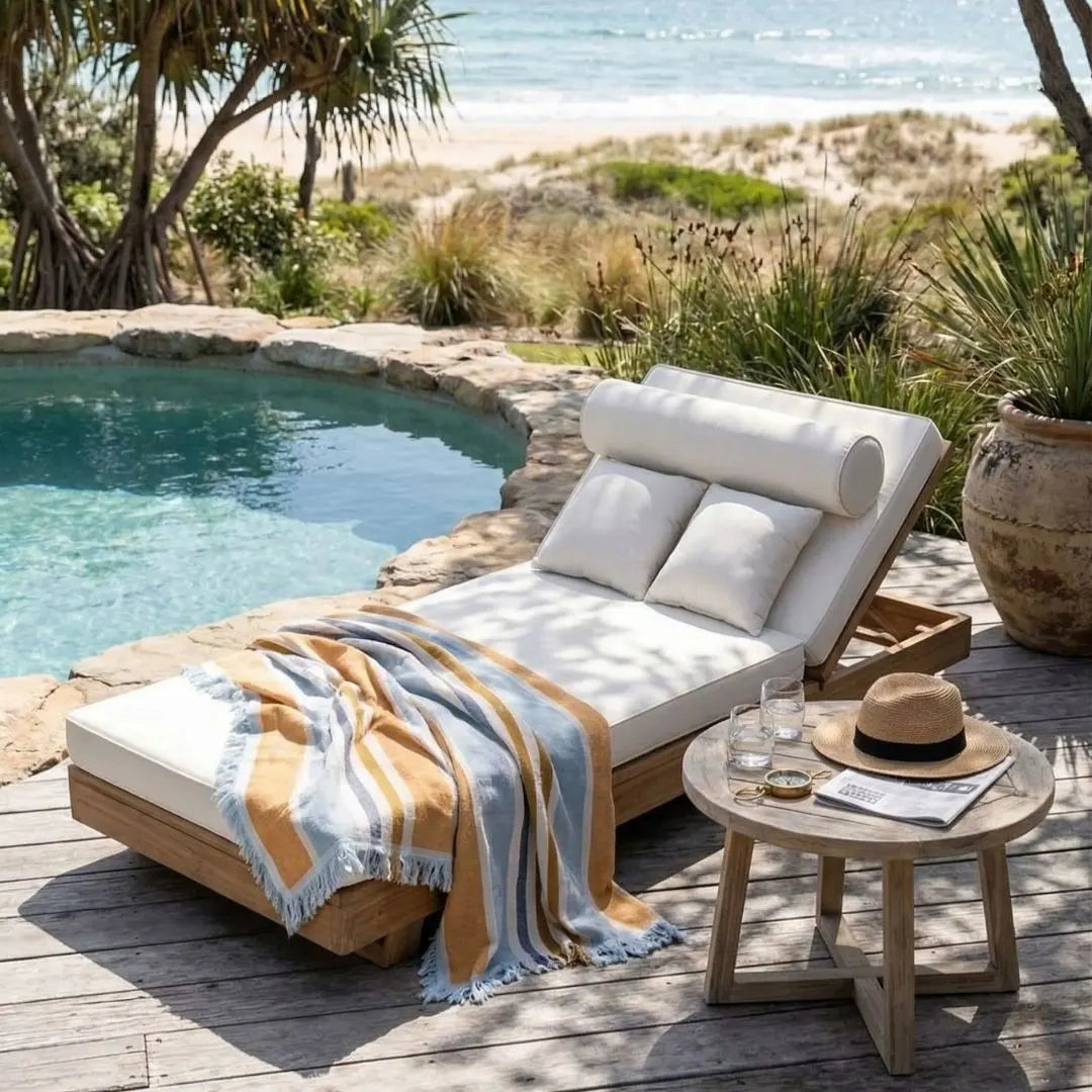 Outdoor lounge chair with cushions and a towel by a poolside with beach view