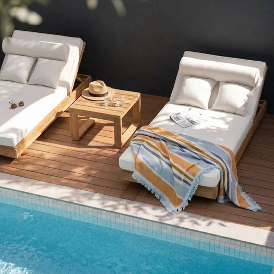 Two white lounge chairs with wooden frames by a poolside on a wooden deck.