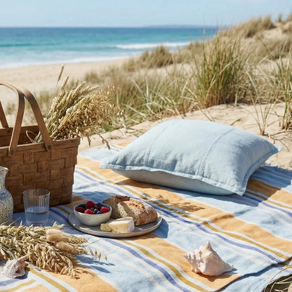 Beach picnic setup with a basket, tablecloth, and food on a sandy beach.