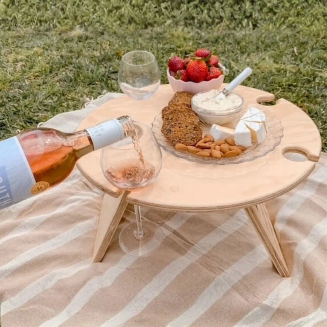 Wooden picnic table with food and wine on a grassy background