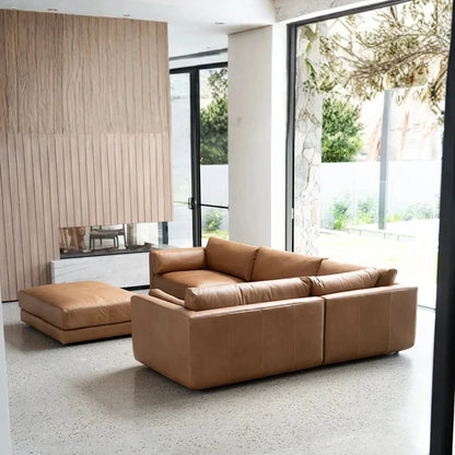 Brown leather sectional sofa in a modern living room with large windows.