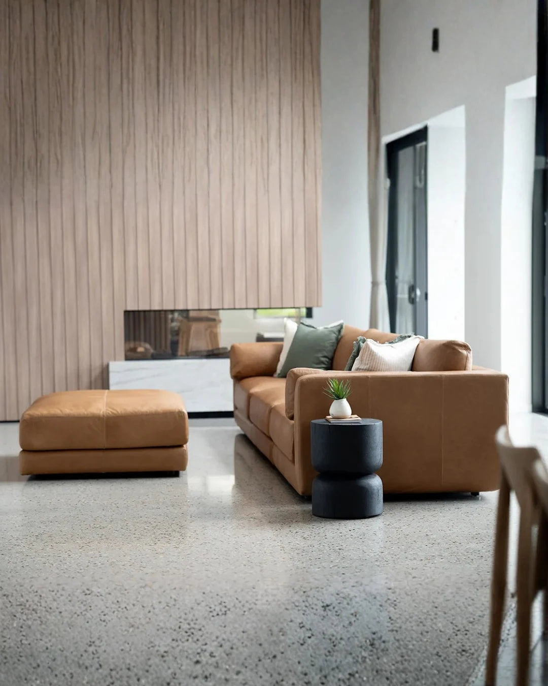 Modern living room with brown sofa, ottoman, and decorative items.