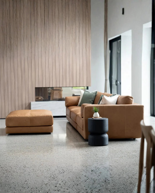 Modern living room with brown sofa, ottoman, and decorative items.