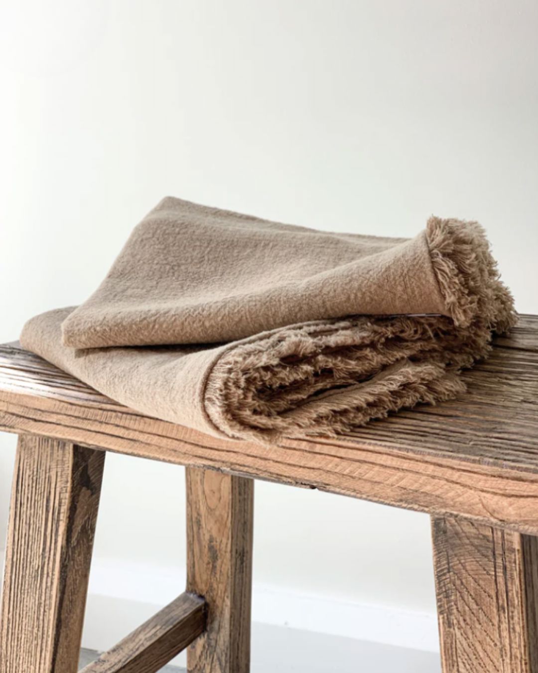 Beige blanket on a wooden stool with a white background