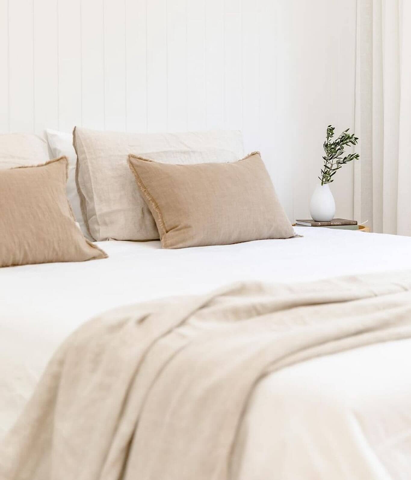 Neatly made bed with beige pillows and blanket in a bedroom setting.