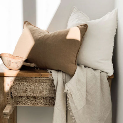 Decorative pillows and blanket on a wooden bench against a white wall