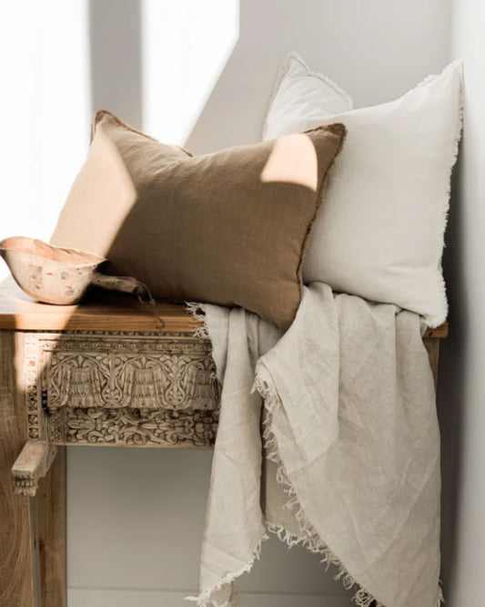 Decorative pillows and blanket on a wooden bench against a white wall