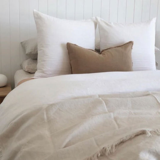 Neatly made bed with white and beige bedding against a white wooden panel wall.