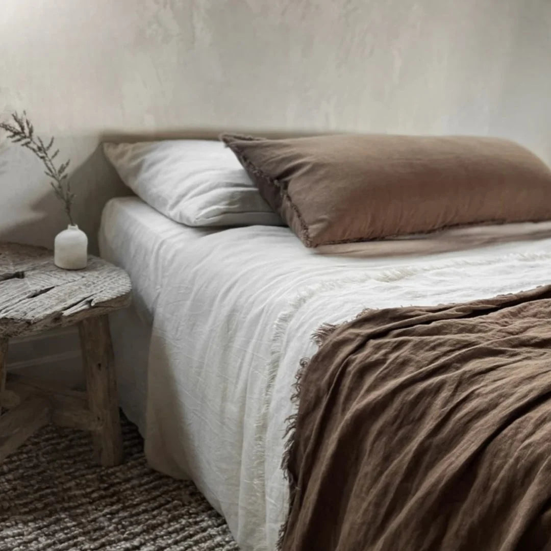 Bed with white bedding and brown pillows in a bedroom setting.