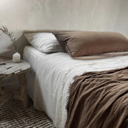 Bed with white bedding and brown pillows in a bedroom setting.