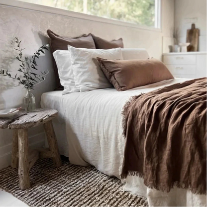 Cozy bedroom with a bed featuring white and brown bedding, a wooden stool, and decorative elements.