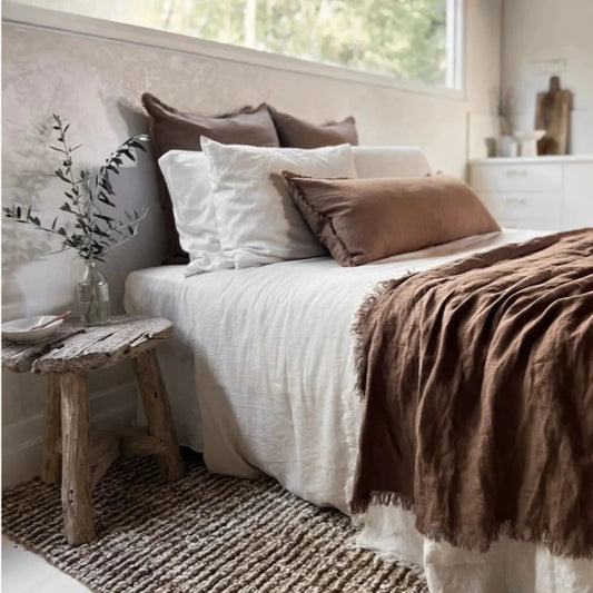 Cozy bedroom with a bed featuring white and brown bedding, a wooden stool, and decorative elements.