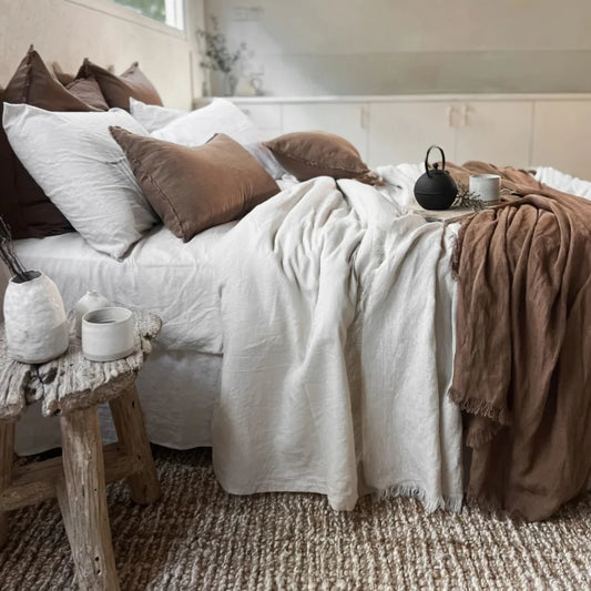 Cozy bedroom with a bed featuring white and brown bedding, a wooden side table, and a small table with a teapot and cups.