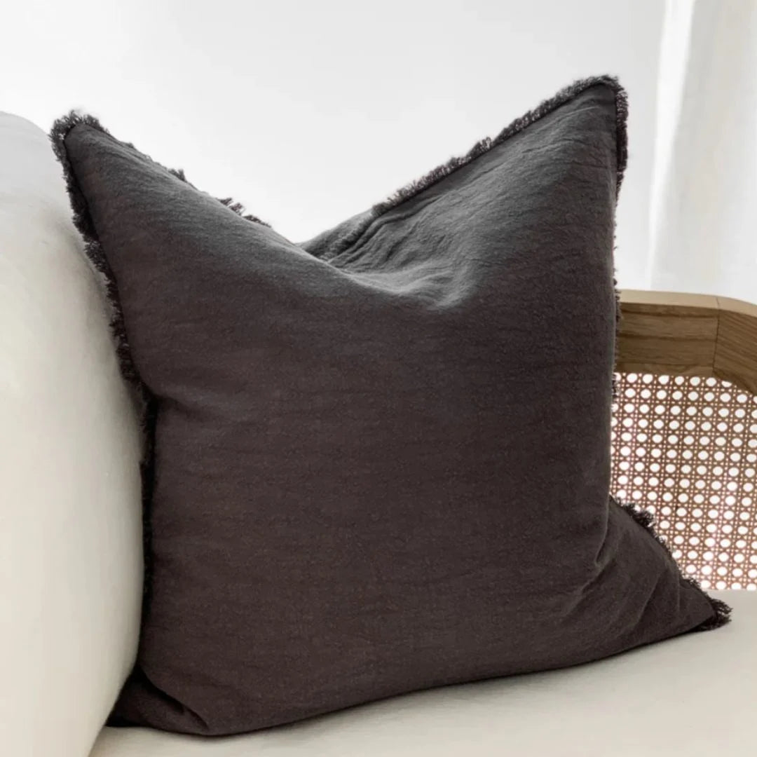 Dark charcoal gray pillow with frayed edges on a light-colored sofa.