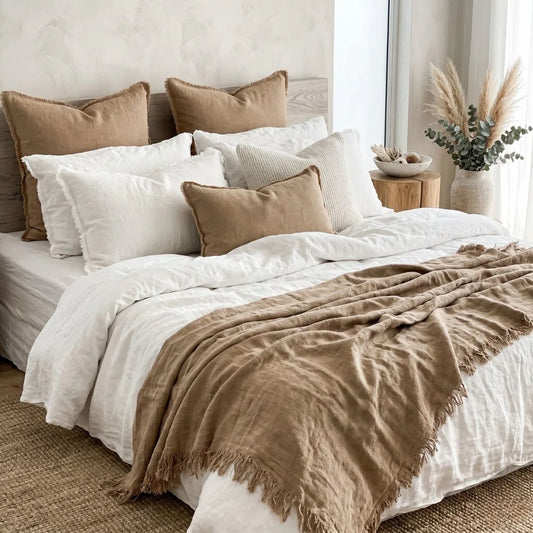 Neatly made bed with white and brown bedding in a bedroom setting.