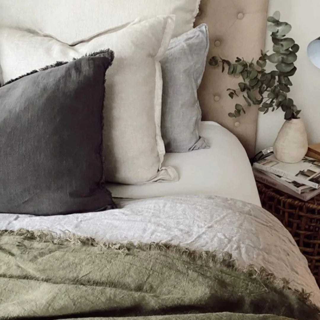 Neatly made bed with decorative pillows and a plant in a bedroom setting