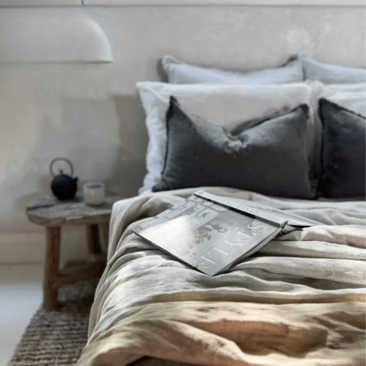 Bedroom with a bed featuring gray and beige bedding, a wooden nightstand with a teapot and candle.
