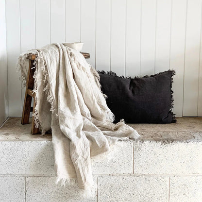 Beige blanket draped over a wooden stool against a white paneled wall.