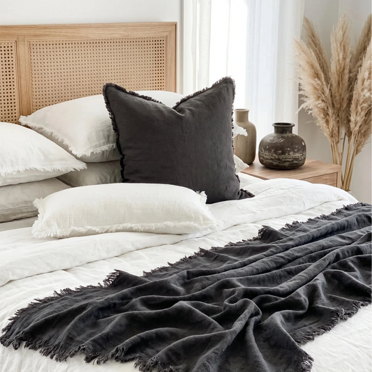 Bed with white bedding, black throw blanket, and pillows in a bedroom setting.