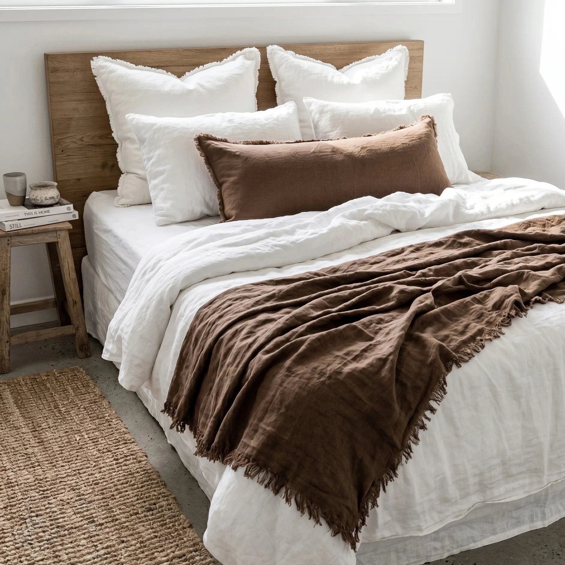 Bedroom with a bed featuring white bedding and brown throw blanket, wooden headboard, and side table.