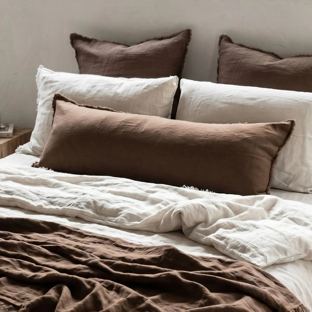 Bed with brown and white pillows and bedding on a neutral background