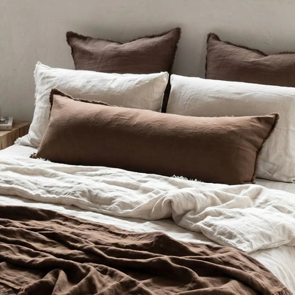 Bed with brown and white pillows and bedding on a neutral background
