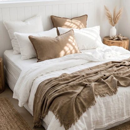 Neatly made bed with white and brown bedding in a bright bedroom.