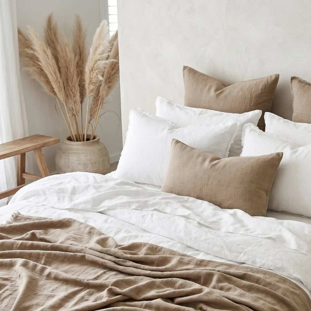 Neatly made bed with white and beige bedding in a bright bedroom.