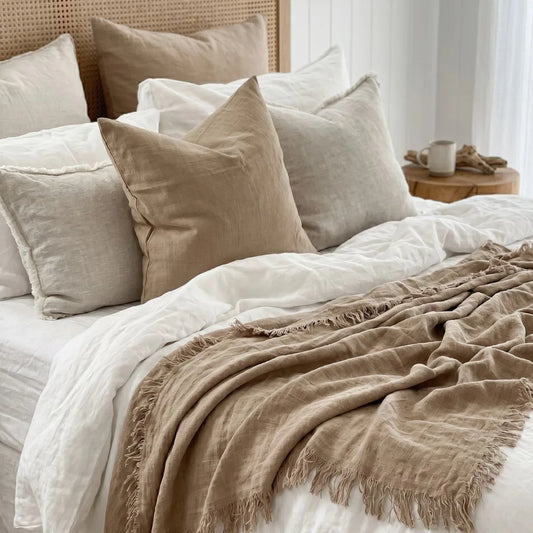 Neatly made bed with beige and white pillows and a blanket in a bright bedroom.