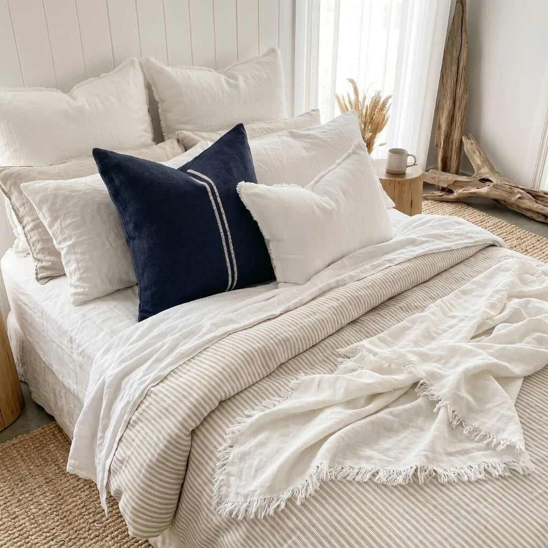 Neatly made bed with white bedding and a blue pillow in a bright bedroom.