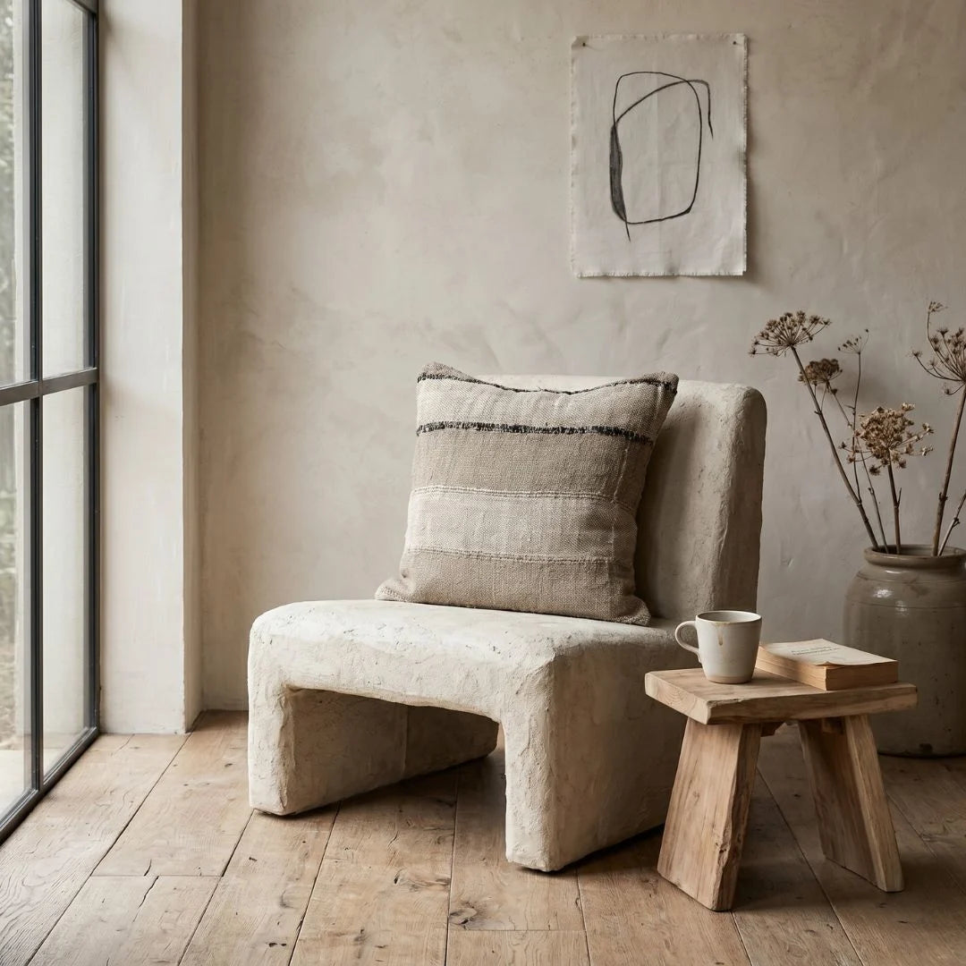 Beige armchair with a pillow in a room with wooden floor and abstract art on the wall.