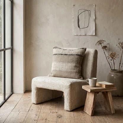 Beige armchair with a pillow in a room with wooden floor and abstract art on the wall.