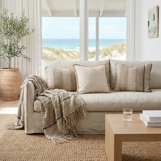 Cozy living room with a beige sofa, throw blanket, and coffee table by a large window with a beach view.