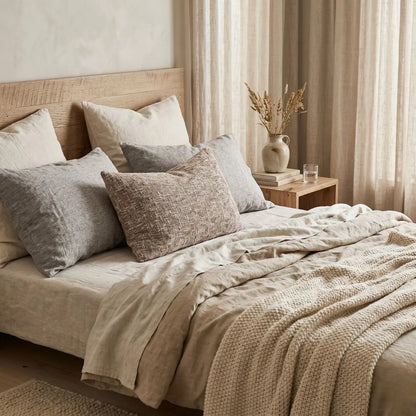 Neatly made bed with decorative pillows and a side table in a bedroom setting.