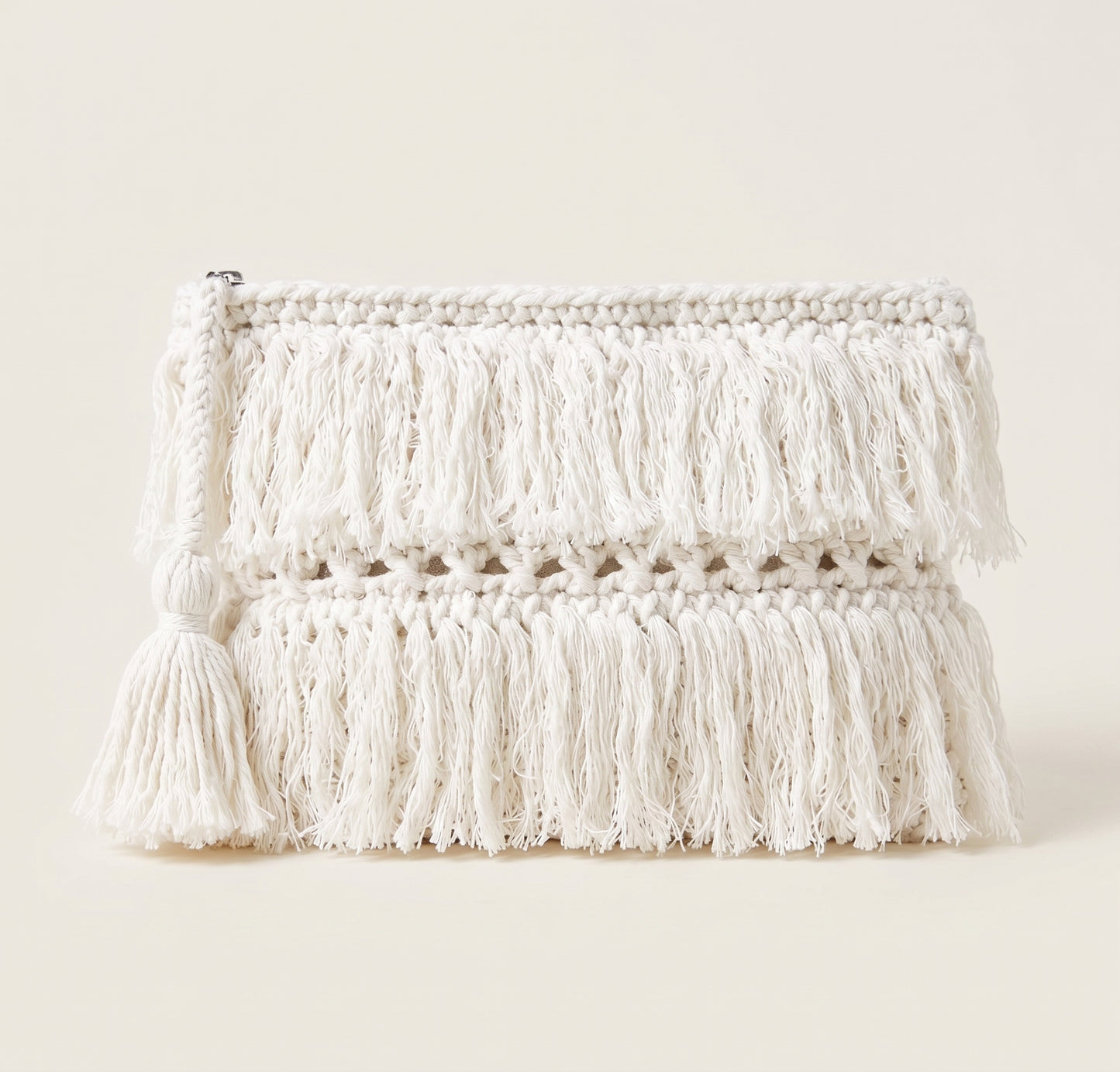 An off-white crocheted clutch bag with multiple layers of fringe tassels and a matching tassel charm, set against a solid cream background.
