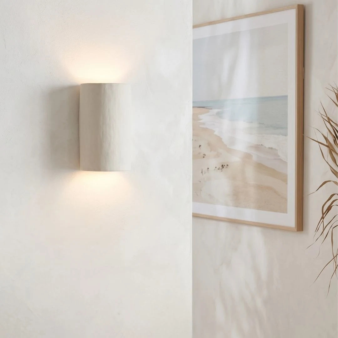 Framed beach scene art on a wall with a lamp and plant