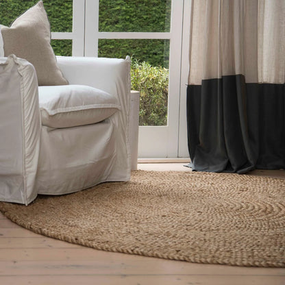 White armchair with beige cushions on a wooden floor, next to a large window with curtains.