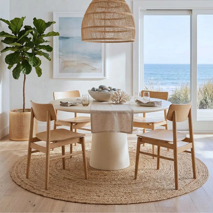 Dining area with a round table and chairs, featuring a beach view through large windows.
