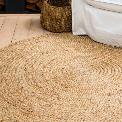 Round woven jute rug on a wooden floor with a basket and bed in the background.