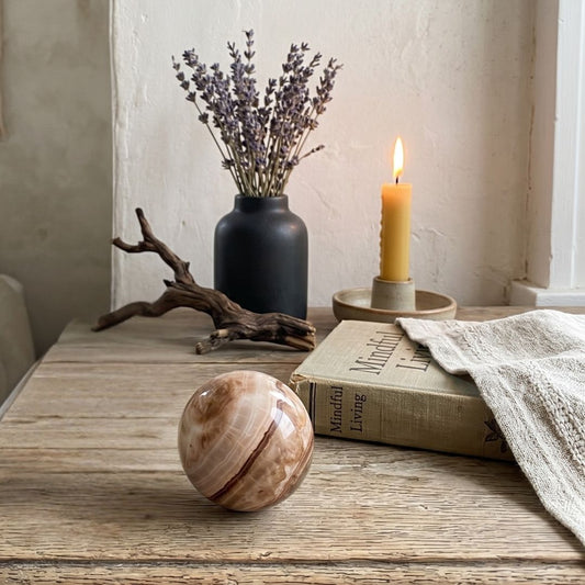 Decorative sphere on a wooden table with a candle, vase of lavender, and book in the background.