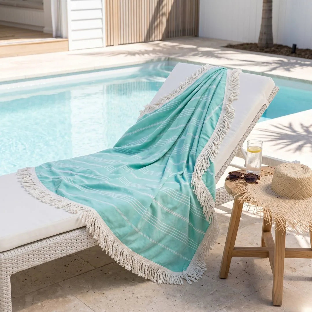 Turquoise towel with white fringe draped over a chair by a poolside.