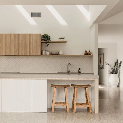 Modern kitchen with wooden stools, white cabinets, and a light-colored floor.