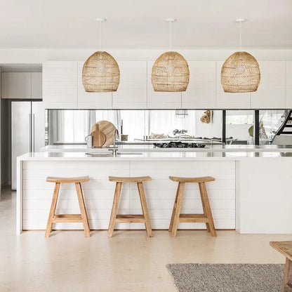 Modern kitchen with white island, wooden stools, and wicker pendant lights.