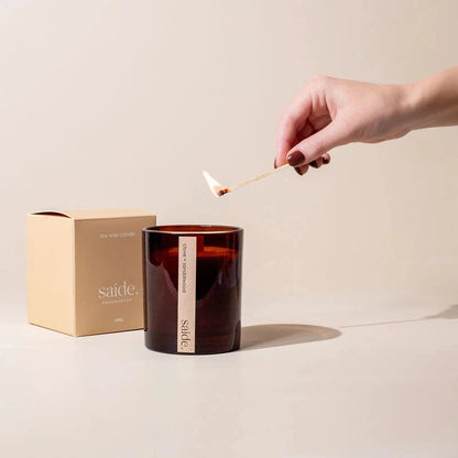 Hand lighting a candle with a 'saide' box in the background on a beige surface