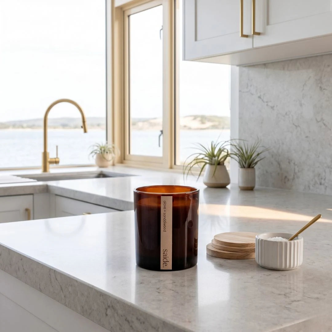 Candle on a kitchen counter with a view of the ocean through a window.