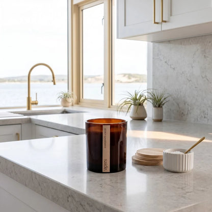 Candle on a kitchen counter with a view of the ocean through a window.