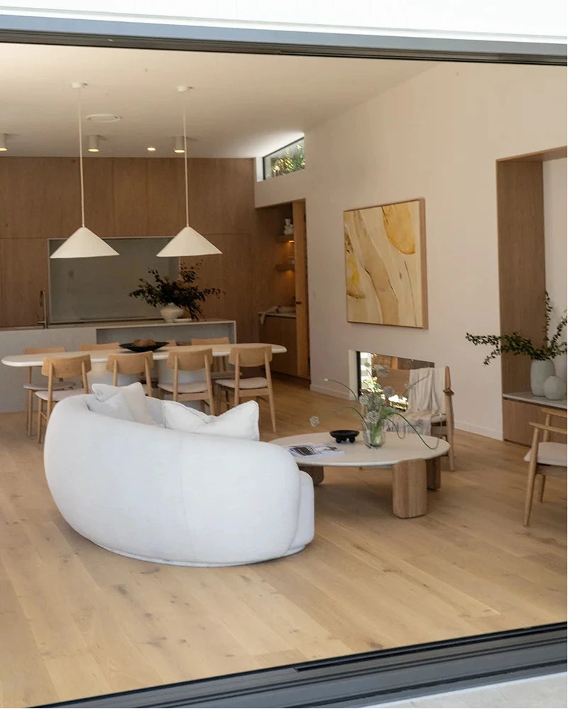 Modern living room with white sofa, wooden floor, and kitchen in the background.
