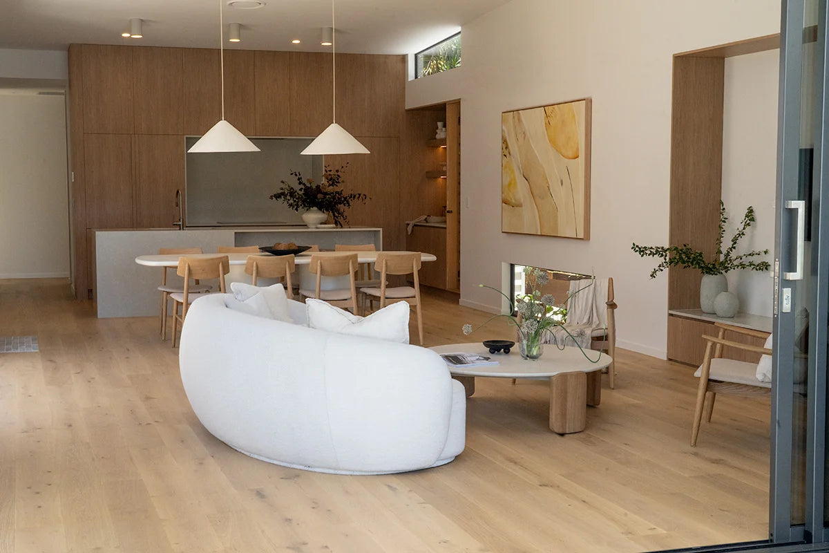 Modern living room with a white sofa, wooden floor, and kitchen area.