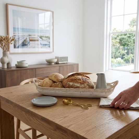 Dining room with a wooden table, bread basket, and a hand reaching out.